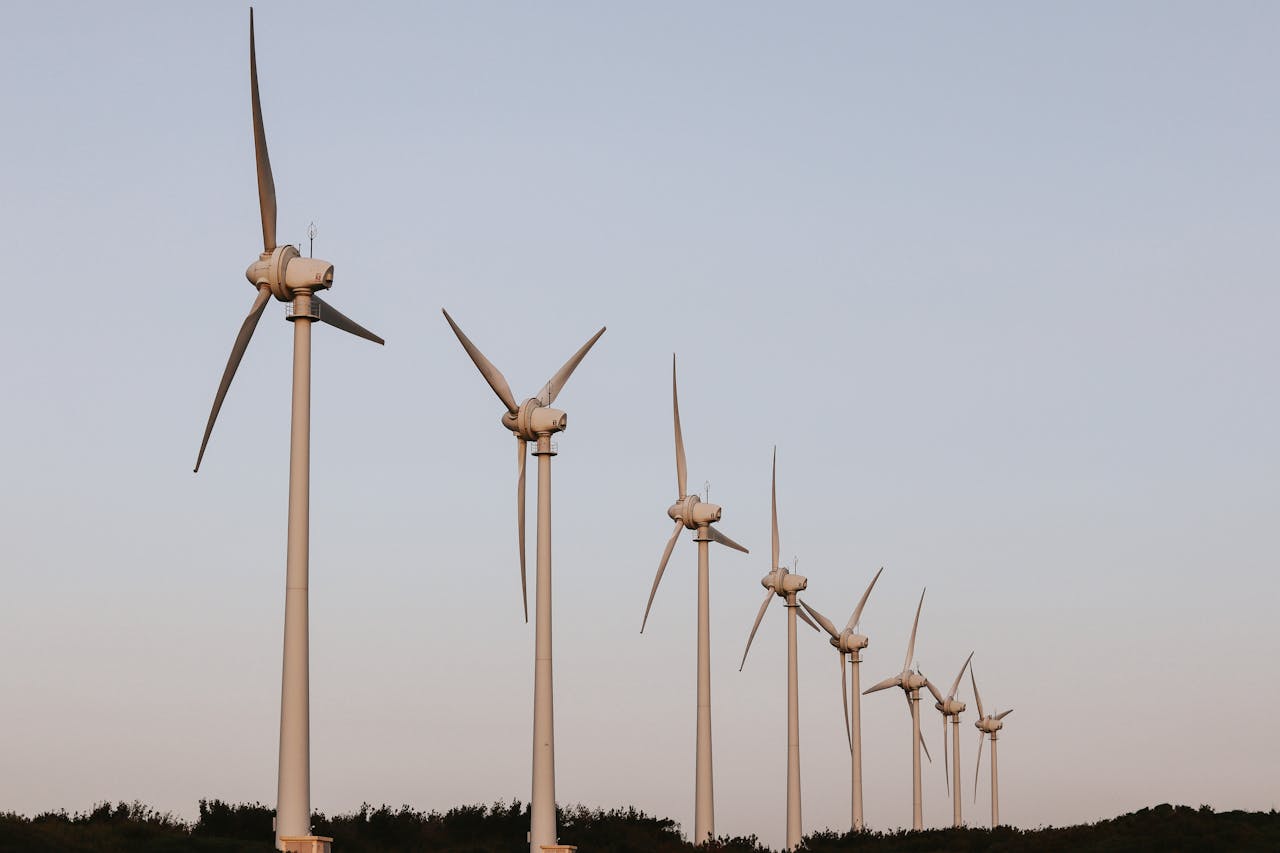 A series of wind turbines stand aligned under a clear blue sky, capturing renewable energy.